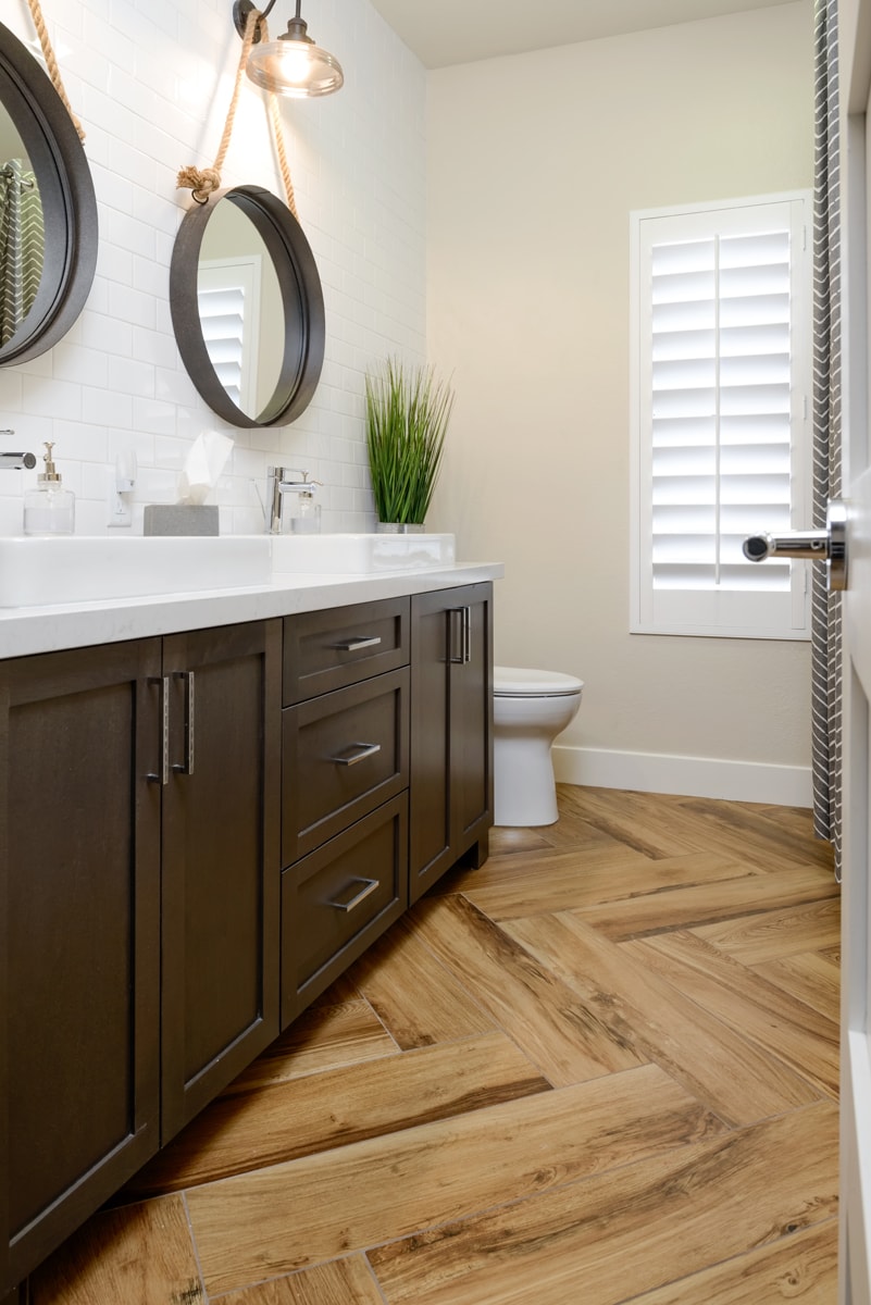 A dark brown bathroom vanity with light wood distresed flooring.