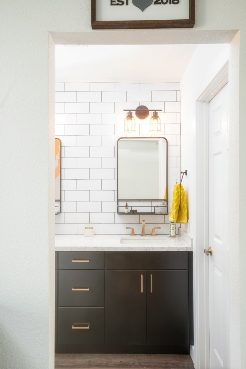 Looking through a doorway, a dark brown vanity with a white countertop and subway tile backsplash.