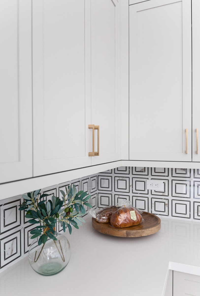 Upper white kitchen cabinets with white geometric tile backsplash.